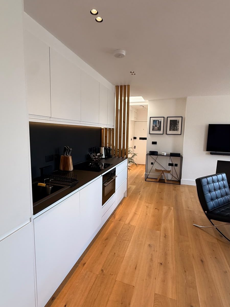 Marylebone kitchen after renovation, with white cabinetry, black splashback and oak floor